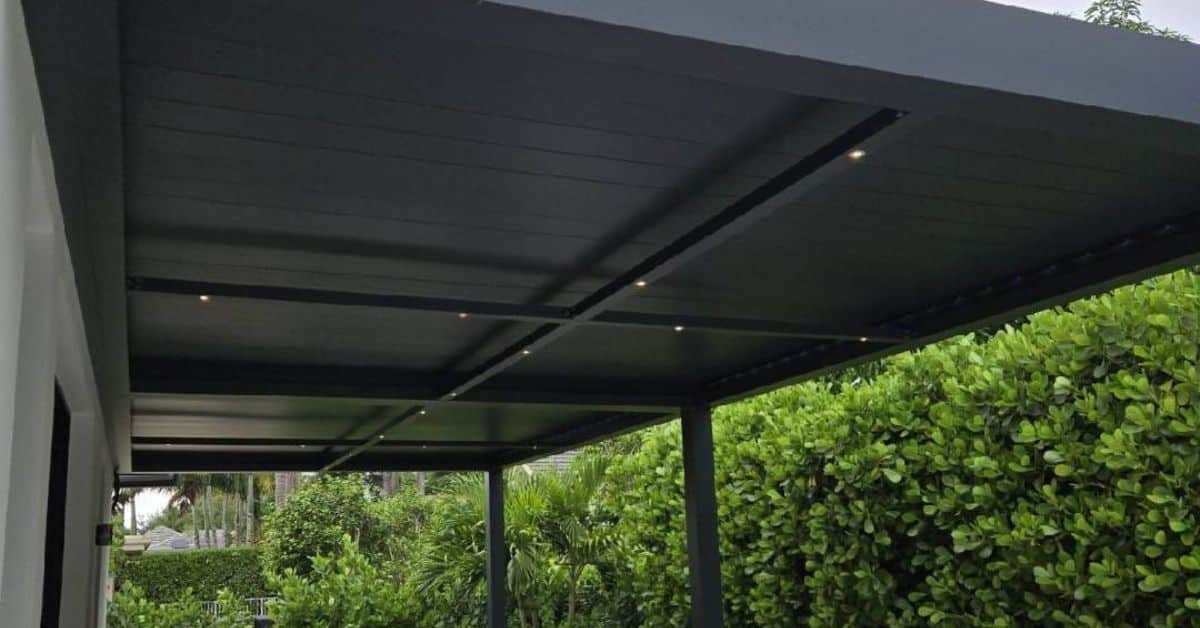 A view of a black louvered pergola ceiling at dusk featuring small, warm recessed LED pot lights installed within the structural crossbeams.